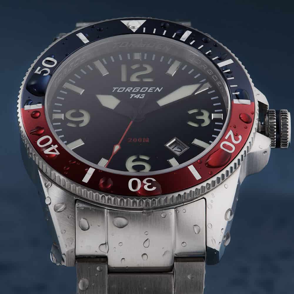 Detailed closeup of a steel watch in sparkling water drops with a vibrant blue red rim featured in a lifestyle product photographer showcase befor